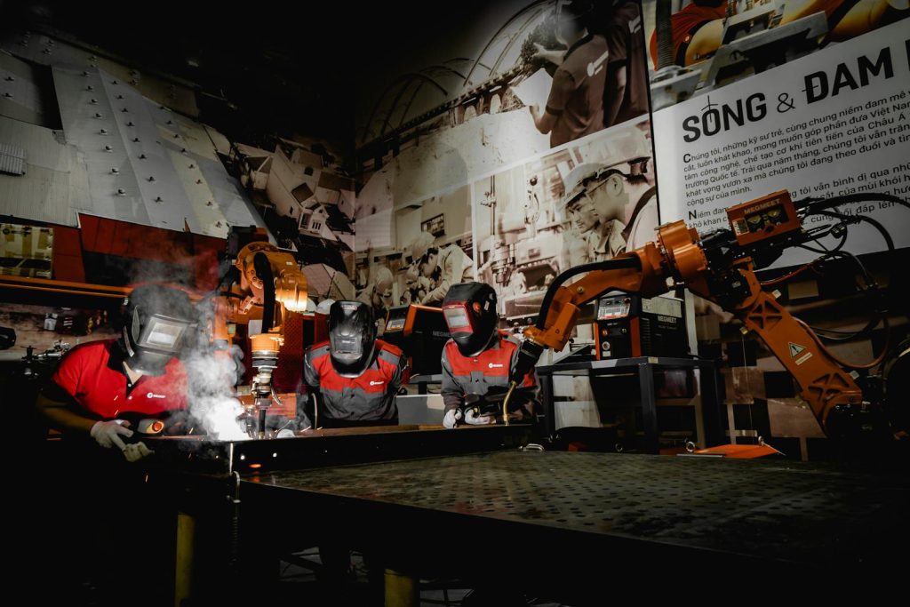 Men in Protective Uniform Welding with Robot in Workshop